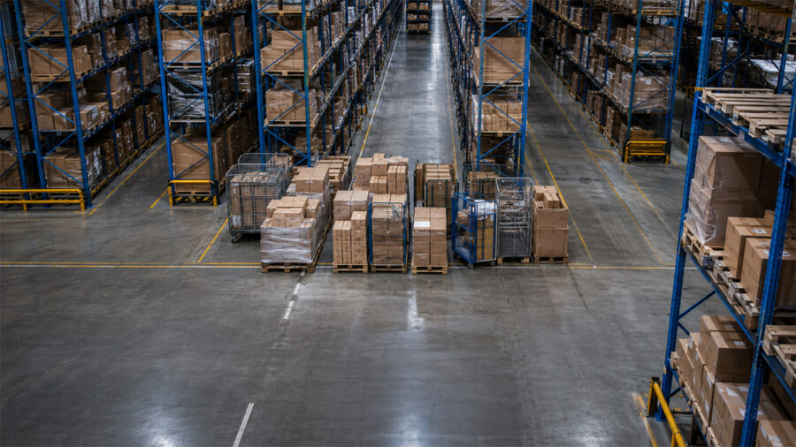 Pallets, cartons and roll cages staged across a warehouse aisle